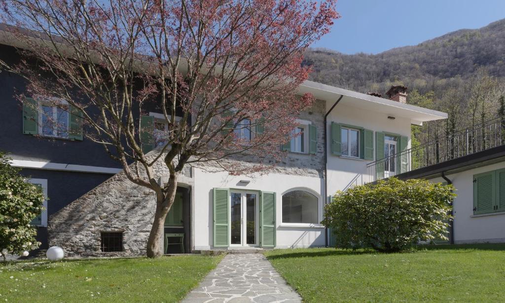 a white house with green shutters and a tree at La casa del lupo in Colico