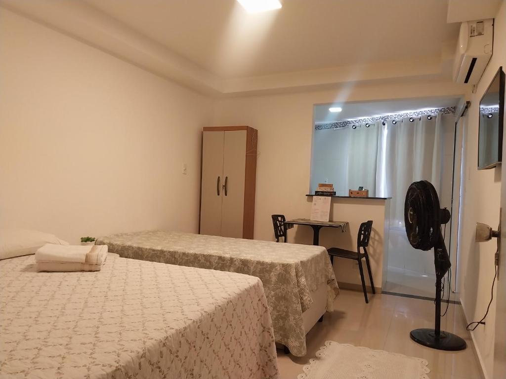 a room with two beds and a table with a chair at Kitnet no Centro Garagem, ar e Wi-Fi in Itaperuna