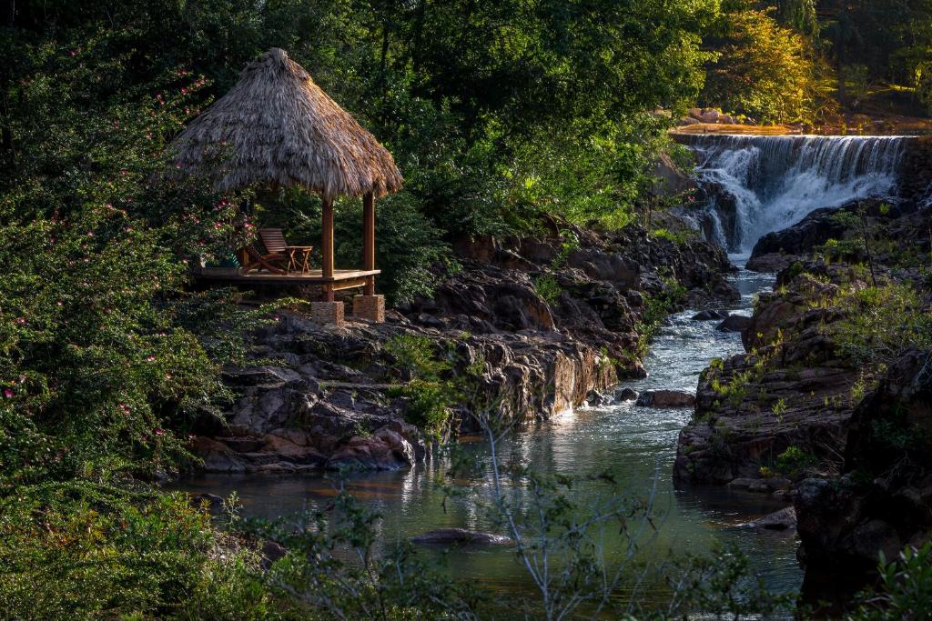 a waterfall with a bench and a hut next to a river at Blancaneaux Lodge in San Ignacio