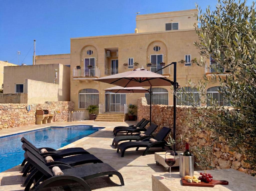a pool with chairs and an umbrella next to a building at Danny House in Nadur