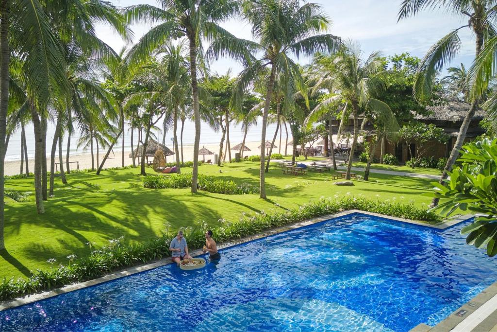 A palm-lined resort pool sits beside a bright tropical beachfront garden.