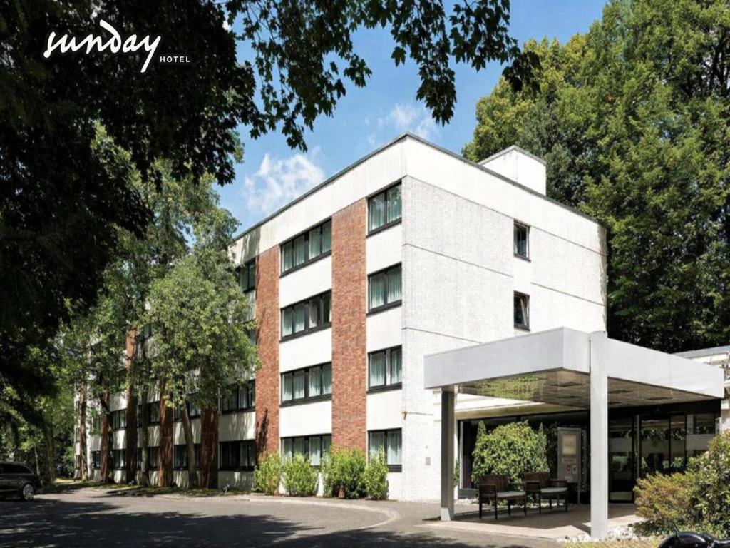 a white building with trees in front of it at Sunday Hotel Bielefeld Standard King Room in Bielefeld