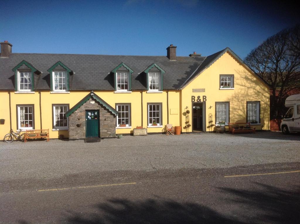 un grand bâtiment jaune avec une voiture garée devant lui dans l'établissement The Old School House B&B, à Baile na Sceilge