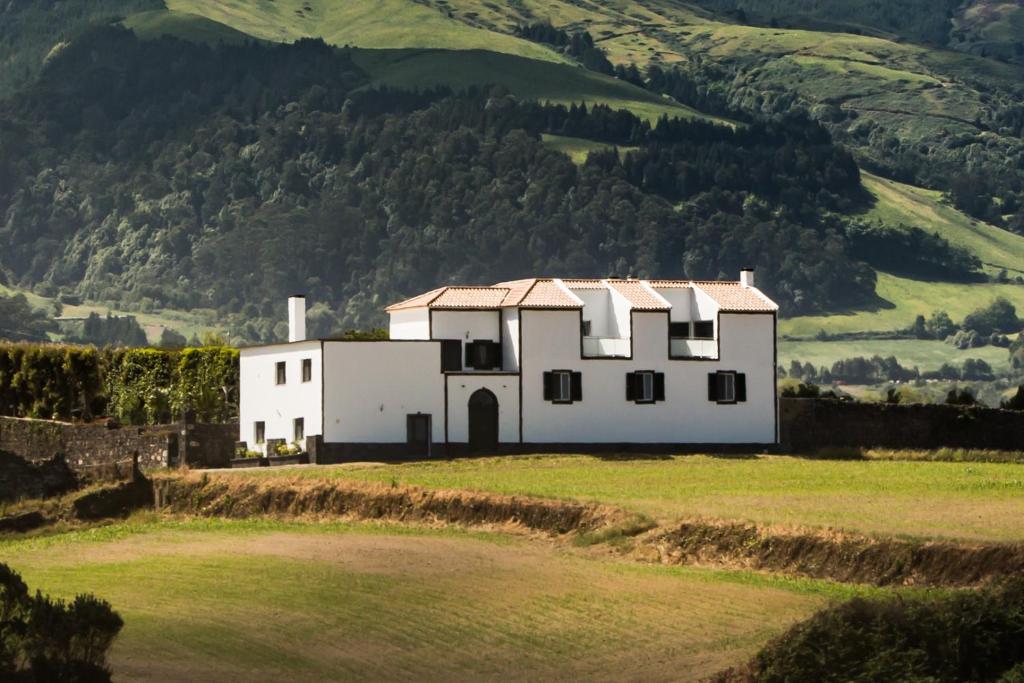 a white house in a field with a mountain at Quinta Velha in Ribeira Grande