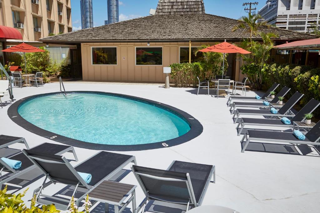 a group of chairs and a swimming pool with chairs and umbrellas at Pagoda Hotel in Honolulu