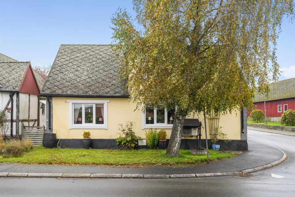 a yellow house with a tree in the street at Österlen - Gathus in Onslunda in Onslunda