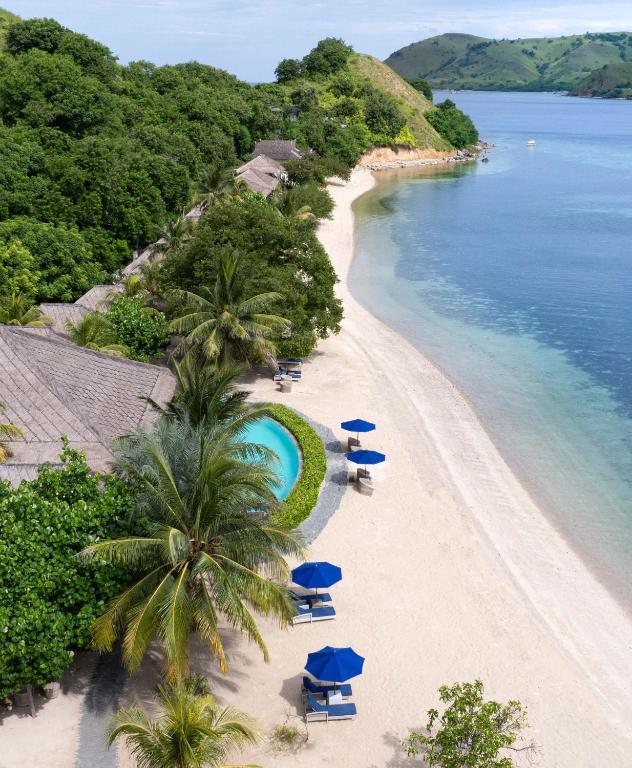 a beach with chairs and blue umbrellas and the ocean at Sudamala Resort, Seraya, Flores in Labuan Bajo