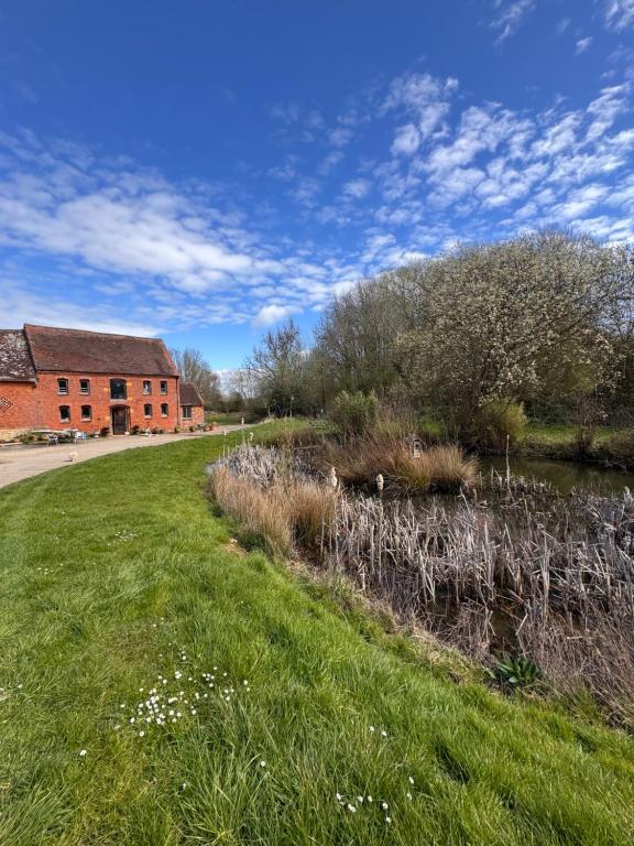 a grassy field next to a brick building and a pond at Fossewold Cotswold Barn in Chipping Campden