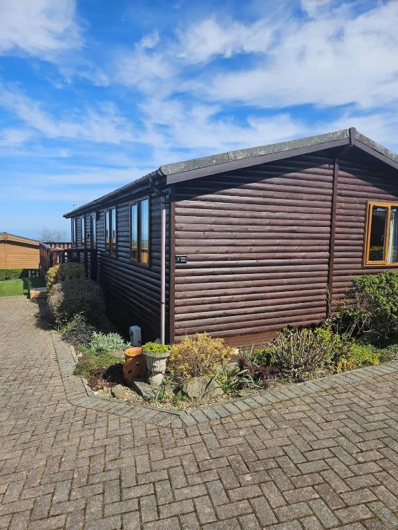 a small wooden cabin with windows on a brick driveway at 3-Bed Ocean View Lodge - Parking & Terrace in Ilfracombe