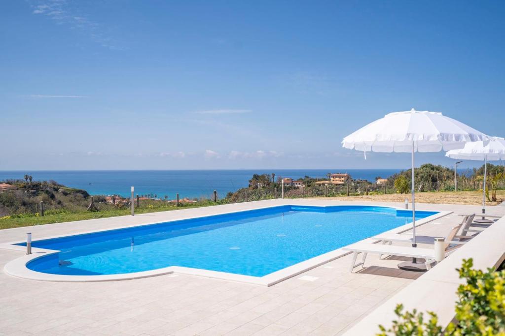 a swimming pool with an umbrella and the ocean at Villa Adele con piscina privata vicino Tropea - per 16 persone in Torre Marino