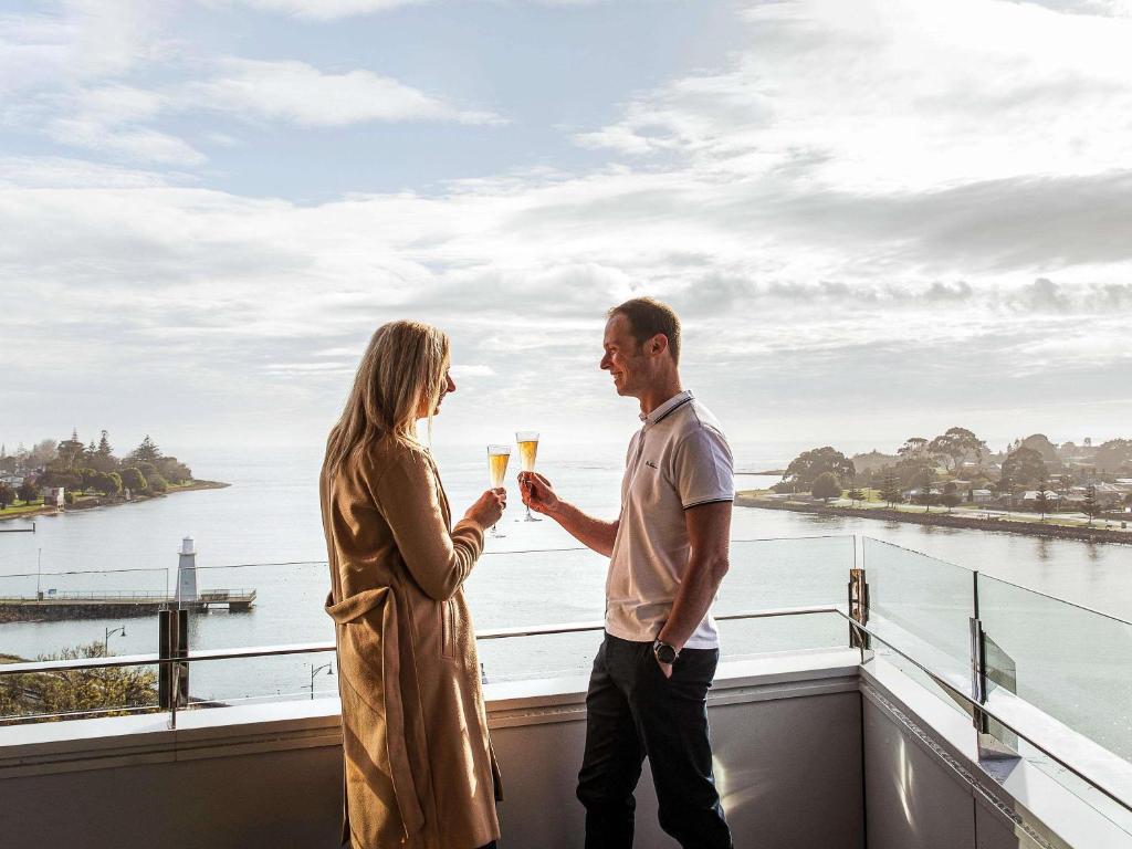 a man and a woman holding glasses of champagne on a balcony at Novotel Devonport in Devonport