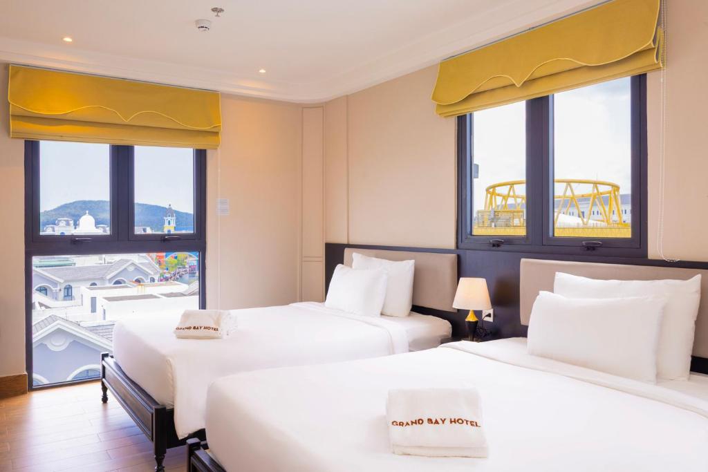 two beds in a hotel room with windows at Grand Bay Hotel - Grand World Phu Quoc in Phú Quốc