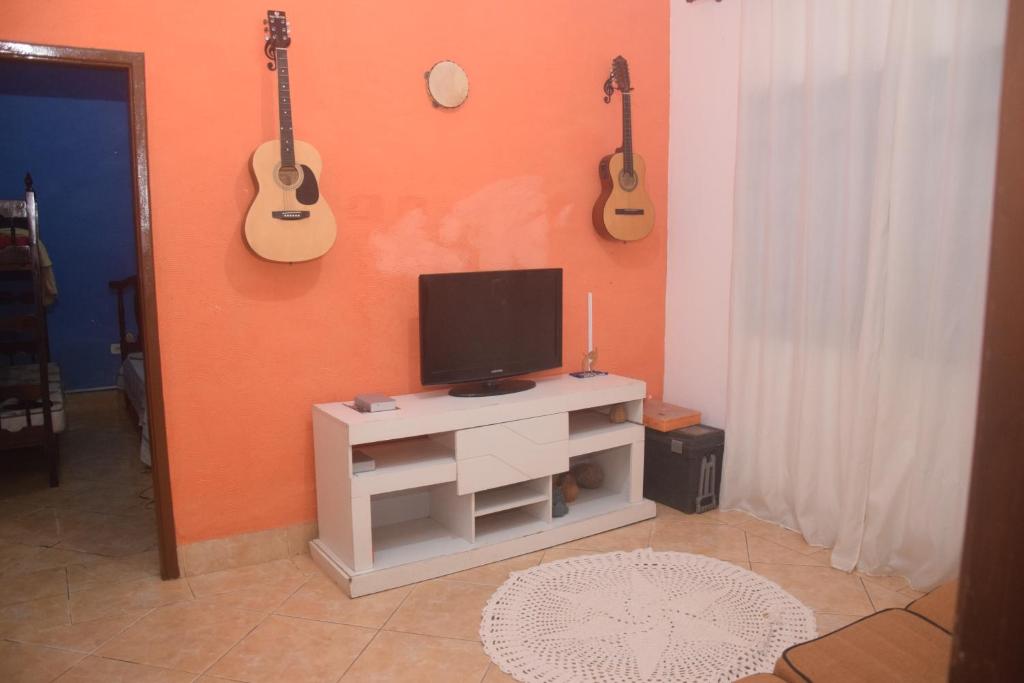 a living room with a tv and guitars on the wall at Conforto e Paz, pertinho do mar! in Caraguatatuba