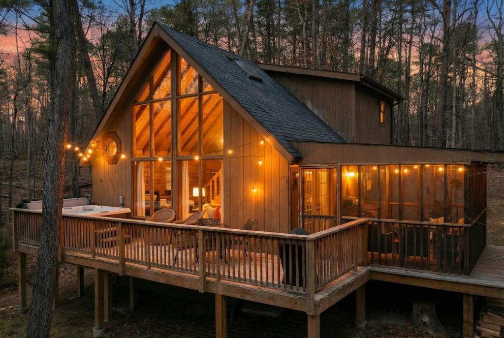 a large wooden cabin with a large deck in the woods at Dog-Friendly A-Frame with Hot Tub and Firepit in Hedgesville