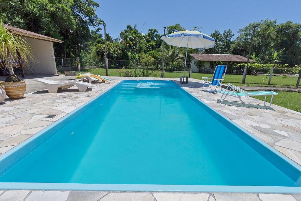 a blue swimming pool with a patio and an umbrella at Chácara Caminho do Rio in Morretes
