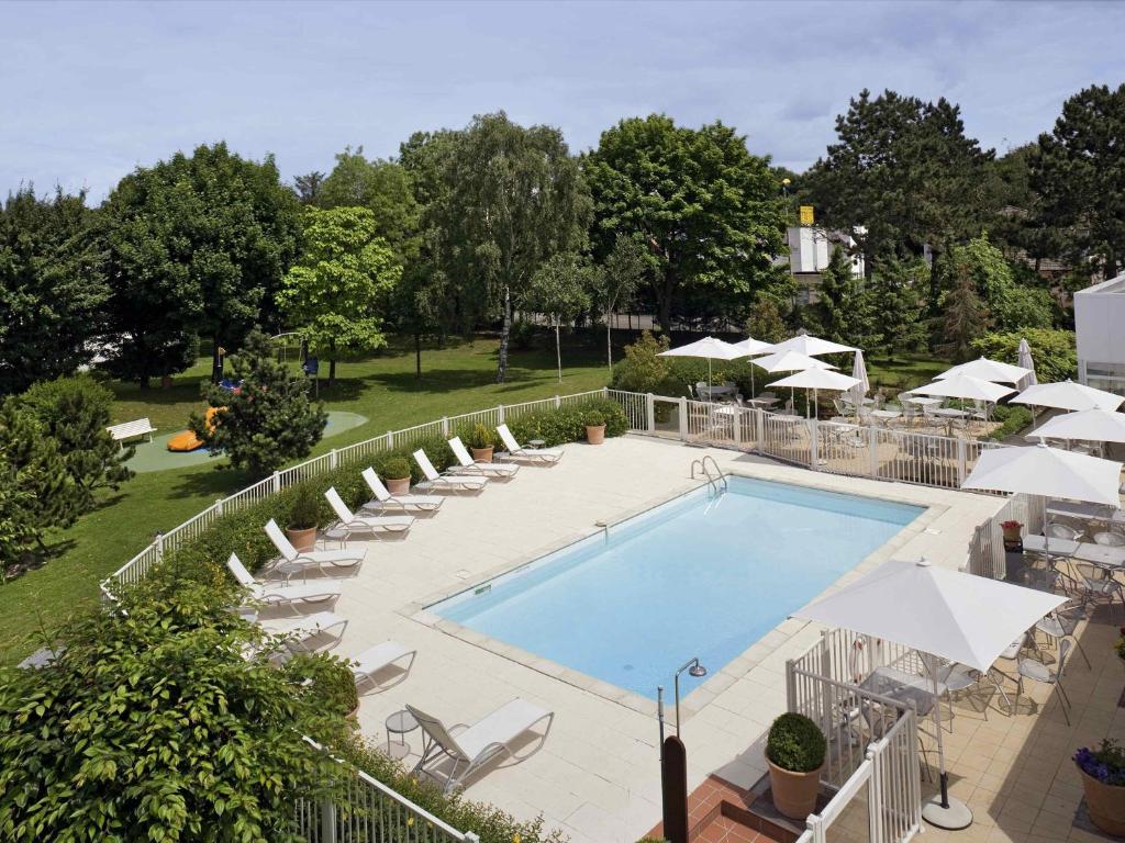 a swimming pool with lounge chairs and umbrellas at Novotel Amiens Pôle Jules Verne in Boves