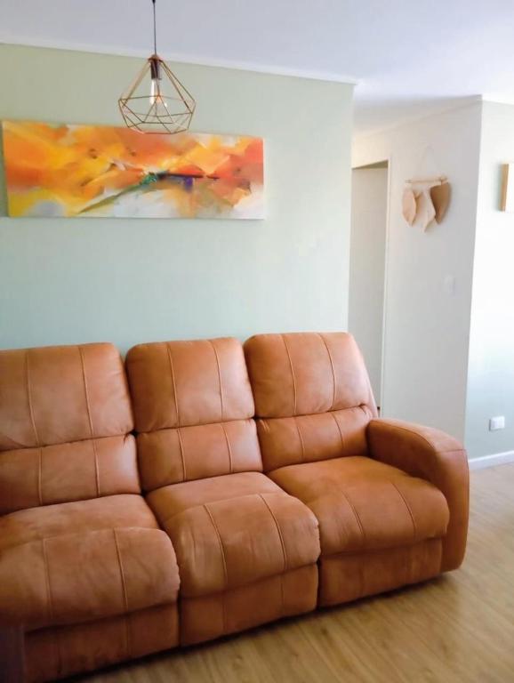 a brown leather couch in a living room with a painting at Departamento El refugio in Osorno