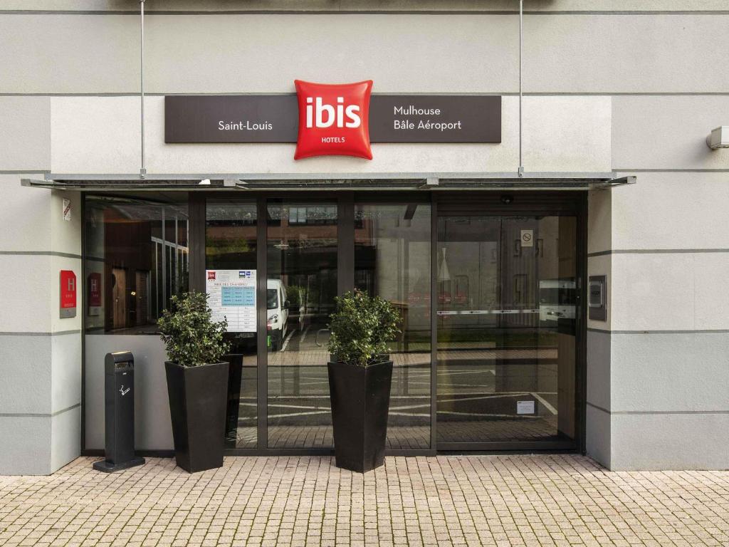 a front door of a building with two potted plants at Ibis Aéroport Bâle Mulhouse in Saint-Louis