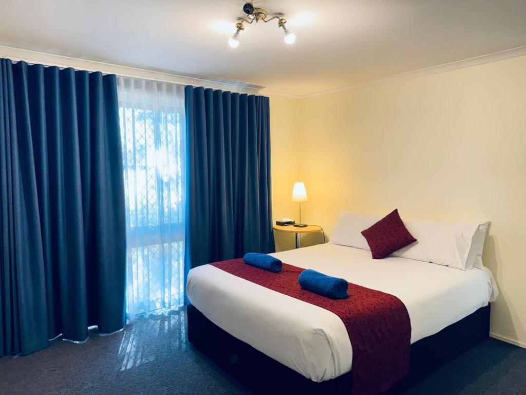 a bedroom with a large bed with blue curtains at Edinburgh Motor Inn in Warragul