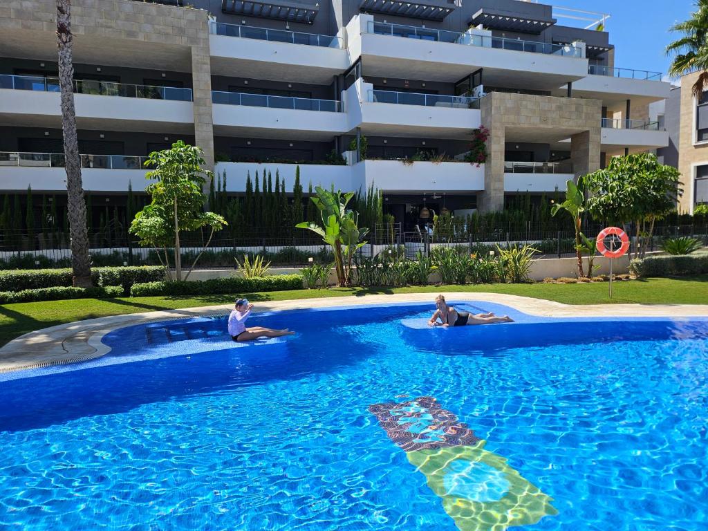 two people sitting in a swimming pool in front of a building at Flamenca Village Resort apt 455 in Orihuela Costa