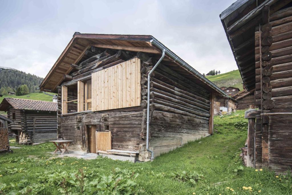 an old log cabin in a field next to a house at Stylish architects hut ski lift in Mutten
