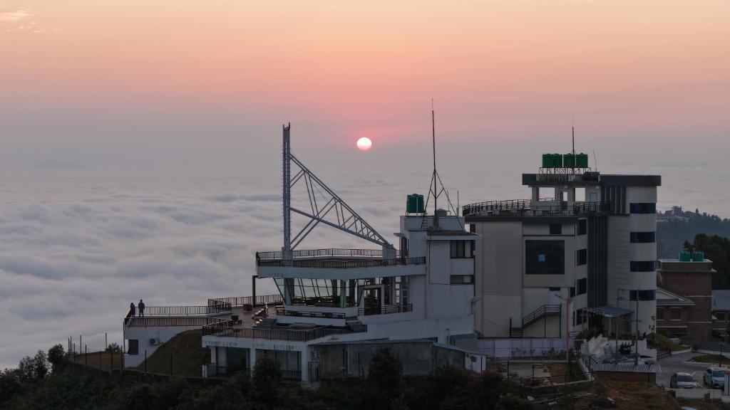 a building on a hill with the sun in the background at Pokhara Heights Resort Pvt Ltd in Pokhara
