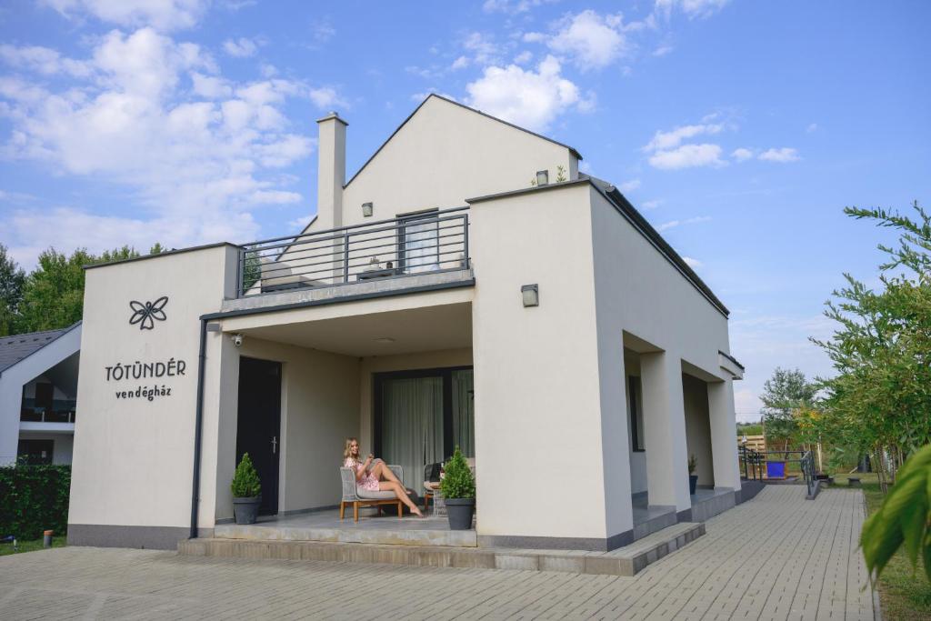a white building with a woman sitting in a chair on the balcony at Tótündér Vendégház in Levelek
