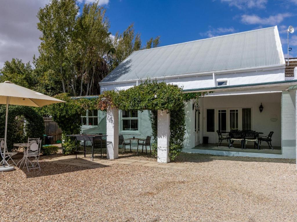 a white house with chairs and an umbrella at Julie's Cottage in Riebeek-Kasteel