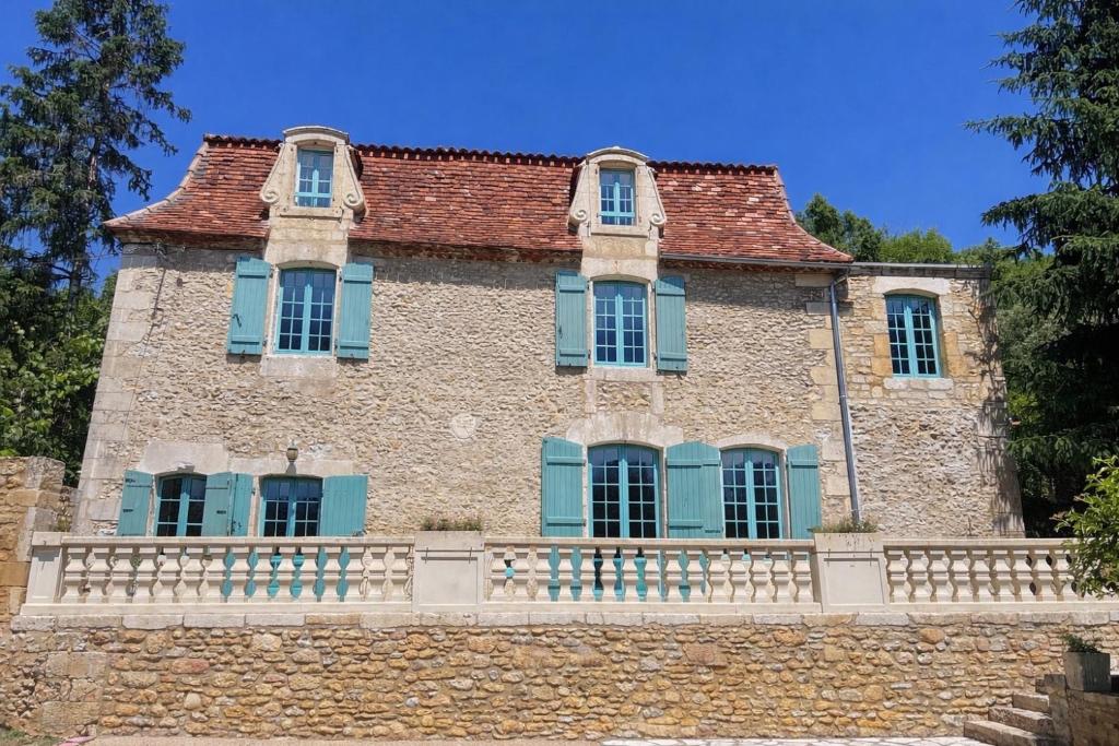 an old stone house with blue windows and a fence at Le Petit Manoir avec Piscine Privée in Le Bugue