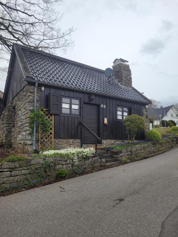 a small black house with a stone wall at Alte Schmiede in Halver