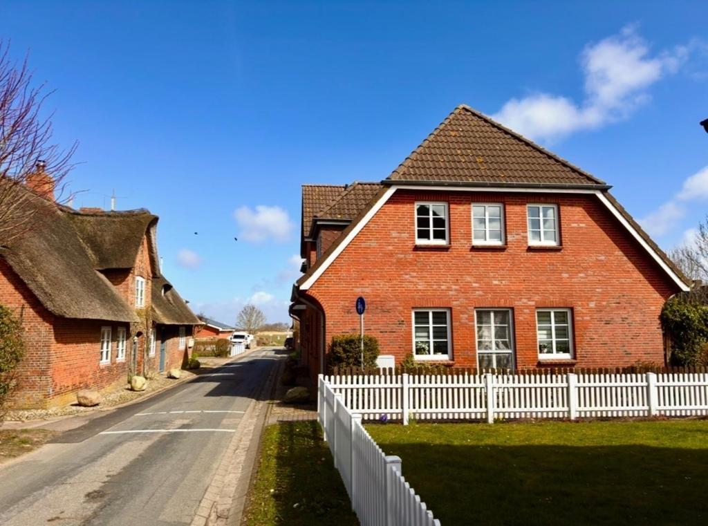 a red brick house with a white fence at Inselglück Föhr in Wrixum