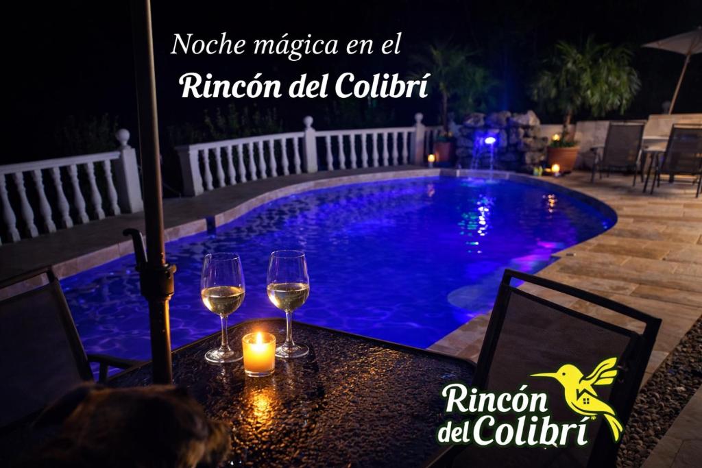 a table with wine glasses and candles next to a swimming pool at Rincón del Colibrí in La Vega