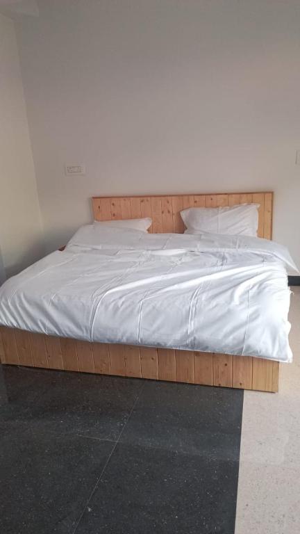 a large wooden bed with white sheets and pillows at Himalayan bite pulga in Kalgha