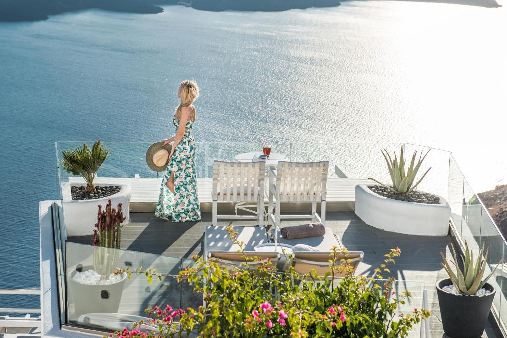 una mujer parada en una cubierta mirando hacia el agua en On The Rocks - Small Luxury Hotels of the World, en Imerovigli