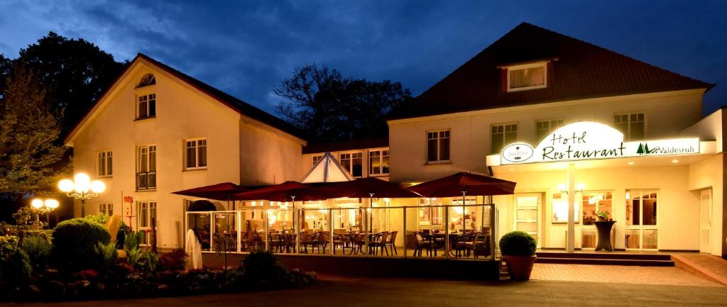 un edificio con un restaurante con mesas y sombrillas por la noche en Hotel Restaurant Waldesruh, en Emstek