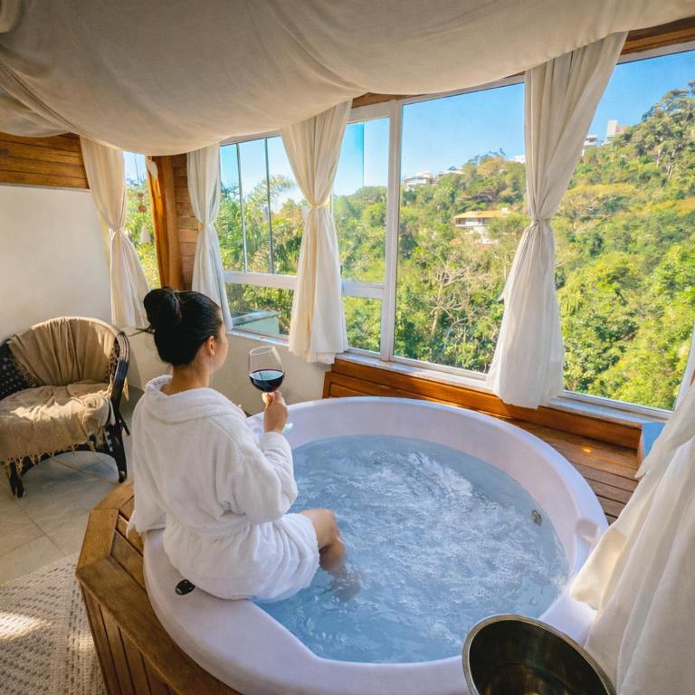 a woman sitting in a bath tub with a glass of wine at Bombinhas Guest House in Bombinhas