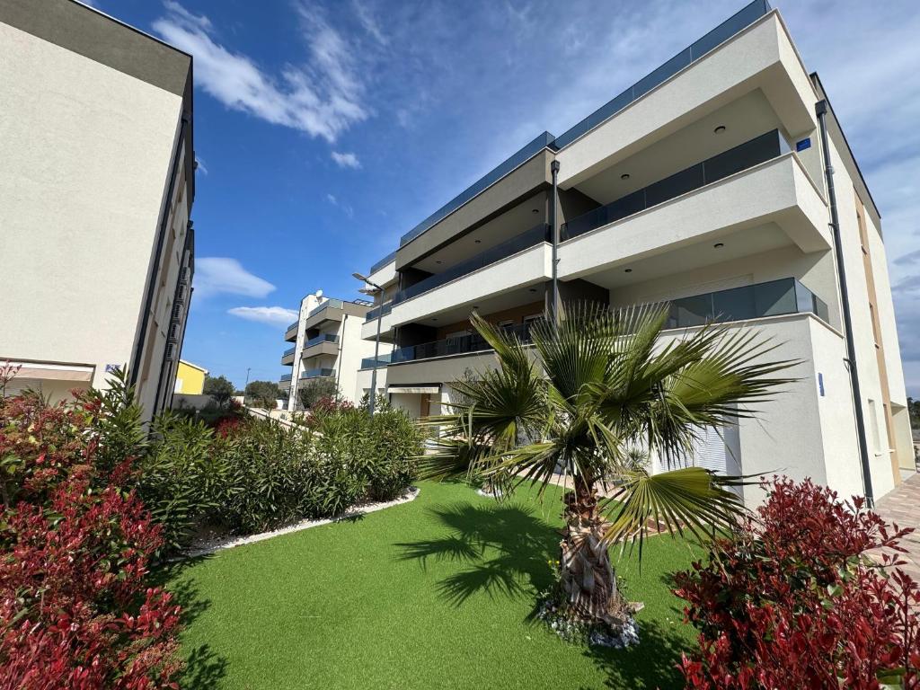 a building with a palm tree in front of a yard at Apartment Lapis with pool near the beach- by TA Leut Agency in Privlaka