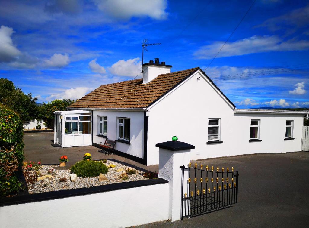 a white house with a gate in a driveway at Woodmount Cottage in Ennistymon