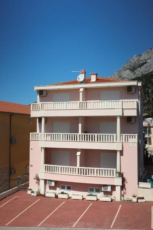 a pink building with a balcony and a parking lot at Apartmani Podest in Baška Voda