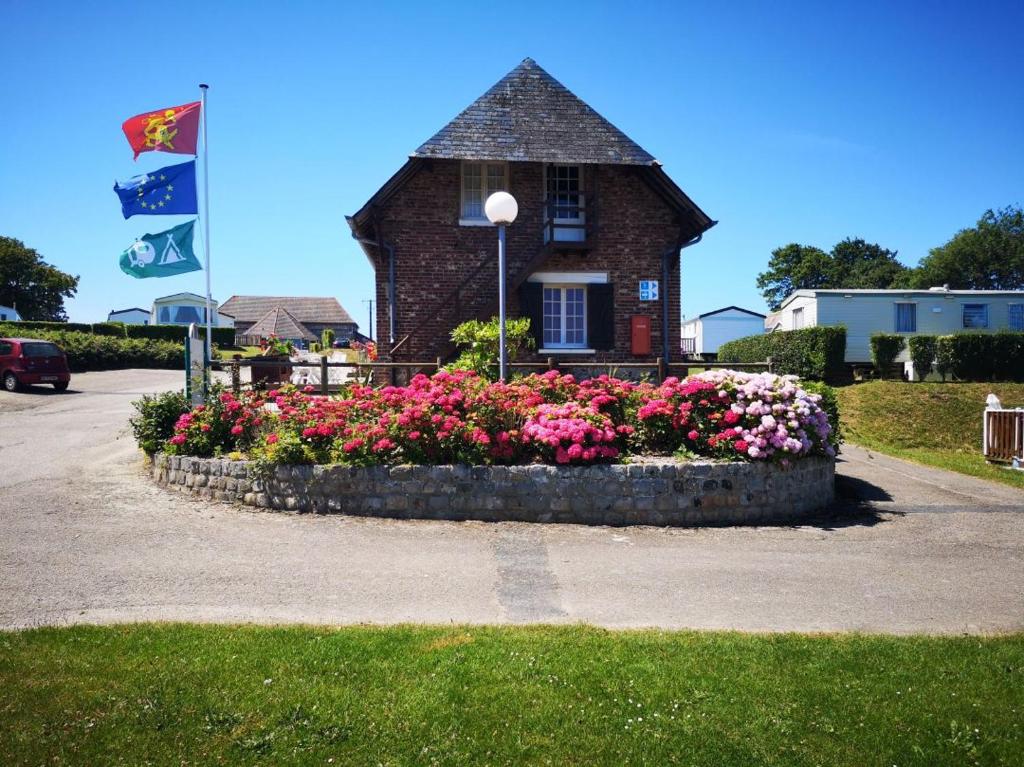 a flower bed in front of a building with a flag at Camping du Mesnil - Gaia Vacances in Saint-Aubin-sur-Mer