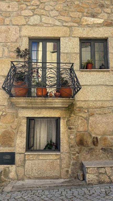 a stone building with three windows with potted plants at Cominhos & Quartilhos in Sortelha