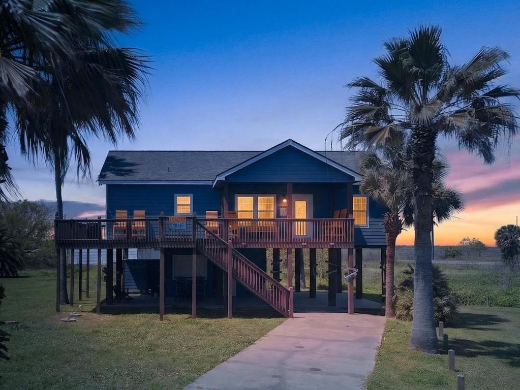 a blue house with a deck and two palm trees at Caribbean Palm Retreat 3BR Near Crystal Beach Fireplace in Bolivar Peninsula