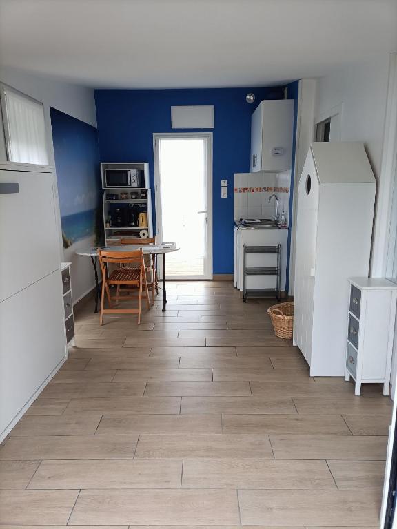 a kitchen with blue walls and a table and refrigerator at Agréable studio indépendant proche mer in Saint-Hilaire-de-Riez