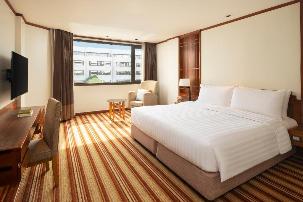 A bright room with a large white bed, window seating and a compact work area.