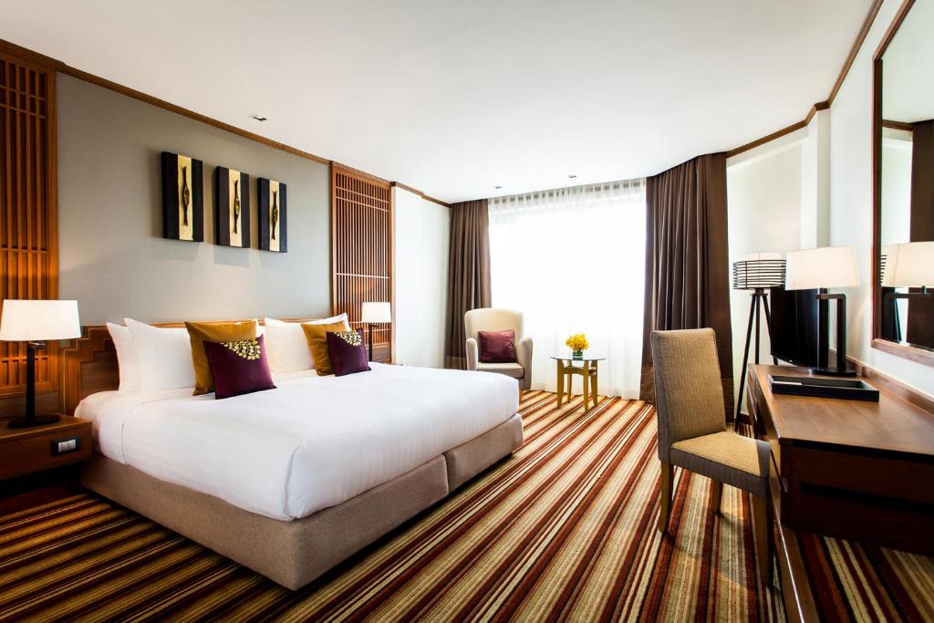 A styled bedroom with a large bed, decorative cushions, seating nook and work desk.