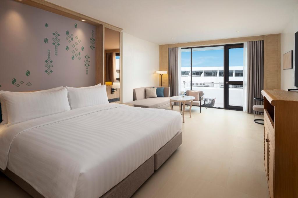 A large bedroom and sitting area with a king-size bed, sofa and full-height window.