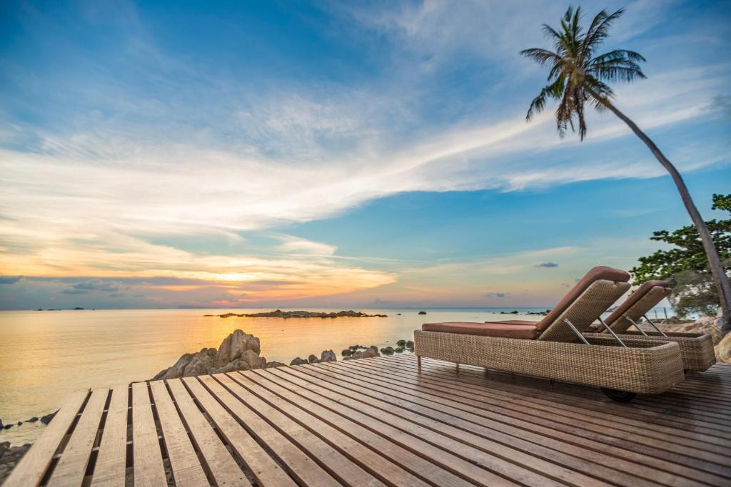 a pair of chairs sitting on a dock with a palm tree at Beyond The Blue Horizon Boutique Bungalows in Haad Chao Phao