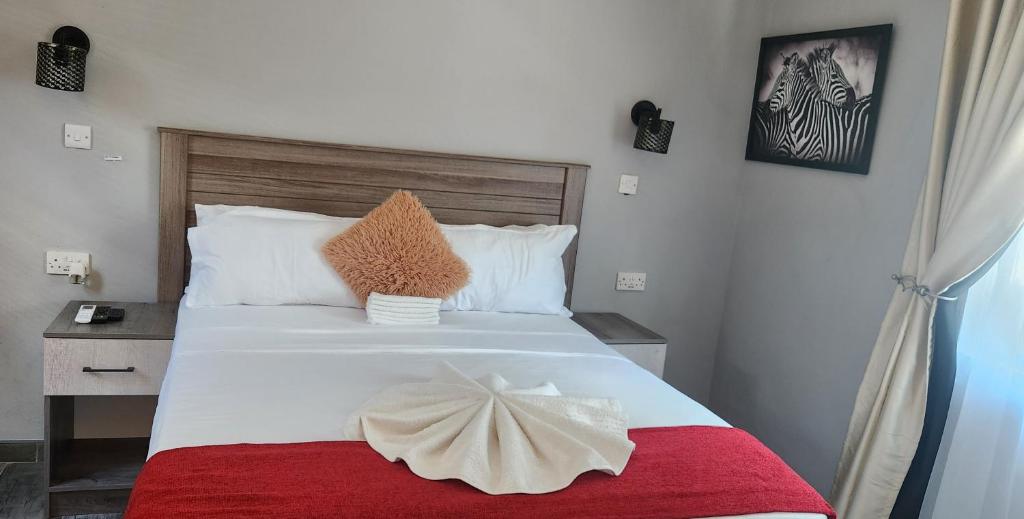 a bedroom with a large white bed with a red blanket at The Hornbill Lodge in Nata