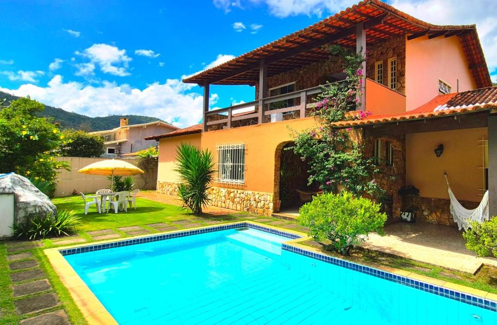 a villa with a swimming pool in front of a house at Suítes Colibri da Serra - Piscina & Conforto em Itaipava RJ in Itaipava