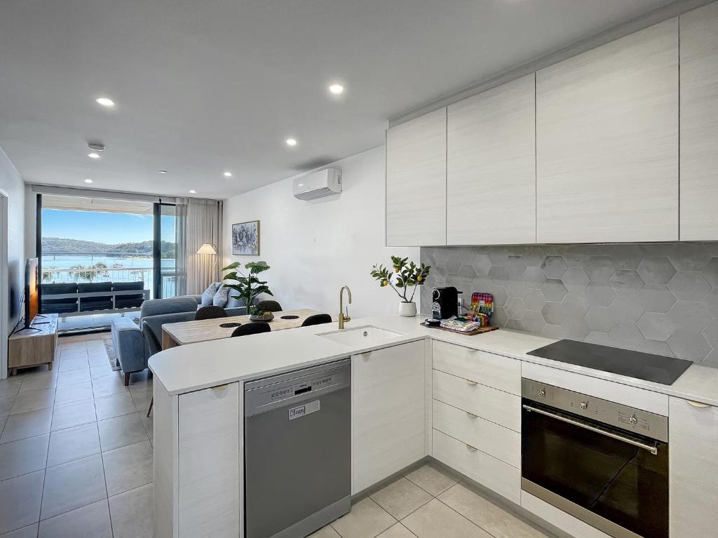 a kitchen with white cabinets and a living room at Bay View 2-Bedroom Apartment in Batemans Bay